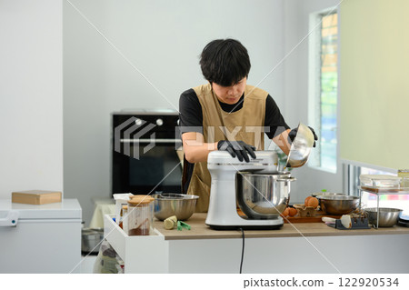 Man wearing black gloves pouring flour into stand mixer while preparing cookie dough 122920534