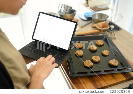 Baker checking recipe on digital tablet while preparing chocolate chip cookie dough 122920539