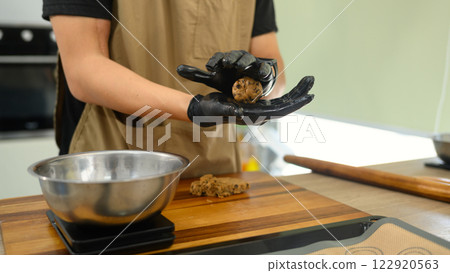 Cropped shot man rolling ball of chocolate chip cookie dough, preparing it for baking 122920563