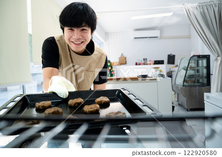 Cheerful small business owner putting a tray of chocolate chip cookies into the oven Cheerful small business owner putting a tray of chocolate chip cookies into the oven 122920580