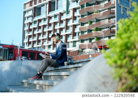 Young businessman with headphones working on digital tablet outdoors in the modern city Young businessman with headphones working on digital tablet outdoors in the modern city 122920598