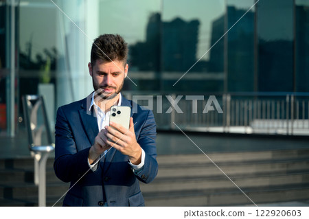 Professional businessman in a suit checking smartphone outside a contemporary office building 122920603