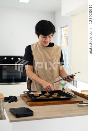 Smiling male baker checking recipe on digital tablet while preparing chocolate chip cookies Smiling male baker checking recipe on digital tablet while preparing chocolate chip cookies 122920612