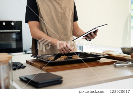 Small business owner checking orders on digital tablet while preparing cookie dough in modern kitchen 122920617