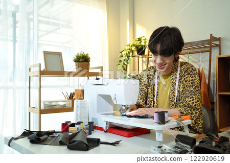 Smiling young designer working on sewing machine in a creative workspace 122920619