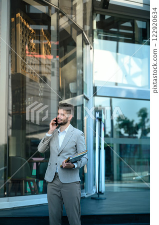 Business executive having a phone conversation outside a glass office building Business executive having a phone conversation outside a glass office building 122920634