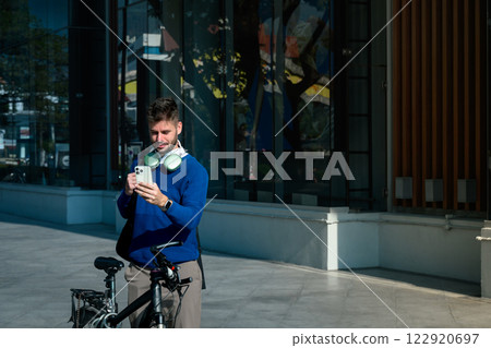 Young caucasian man using smartphone while standing next to his bicycle in the city. Sustainable commuting concept 122920697