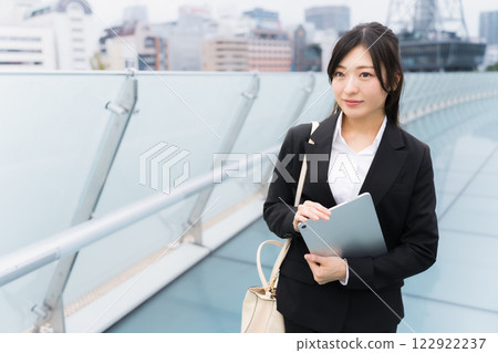 A businesswoman wearing a suit and holding a tablet in an office district 122922237