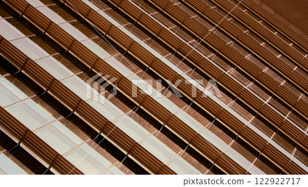 Detailed view of a building facade with a dynamic pattern of diagonal, ribbed metallic panels and reflective glass, creating a sense of depth and texture. 122922717
