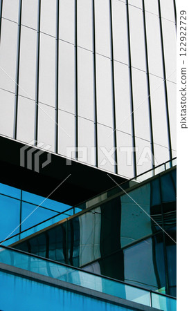 a modern building with sleek vertical lines and reflective blue glass. The light-toned wall above contrasts sharply with the glass windows below 122922729