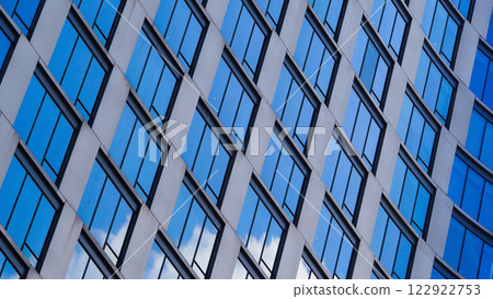 A dynamic diagonal pattern of reflective glass windows creates a sleek, modern aesthetic. The blue sky reflections add depth and contrast to the architecture. 122922753