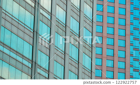 A close-up of modern architecture showcasing contrasting glass facades, blending blue and beige tones with clean geometric patterns. A close-up of modern architecture showcasing contrasting glass facades, blending blue and beige tones with clean geometric patterns. 122922757