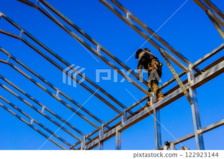 Worker balances carefully on steel beams while constructing commercial building framework 122923144