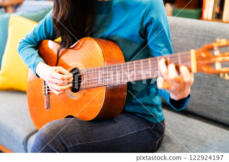Young woman practicing guitar in the living room, no face 122924197