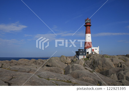 Red and white cast iron Eigeroy Lighthouse,  rock formations and Nort Sea, Norway. 122925395
