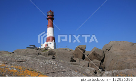 Blue sky over the red and white cast iron Eigeroy Lighthouse and anorthosite rock formations, Norway. Blue sky over the red and white cast iron Eigeroy Lighthouse and anorthosite rock formations, Norway. 122925396
