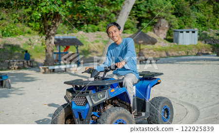 Young Man Smiling on Blue ATV Quad Bike at Sandy Beach Resort 122925839