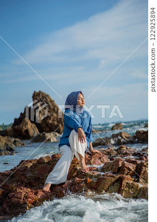 Woman in Hijab Meditating on Rocky Beach Serene Ocean View Relaxation Vacation Woman in Hijab Meditating on Rocky Beach Serene Ocean View Relaxation Vacation 122925894