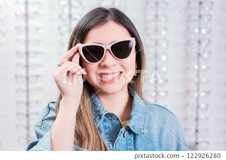 Beautiful girl trying on glasses in an eye store. Smiling female customer trying on glasses in eye shop 122926280