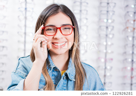 Happy teen girl in eyeglasses on a background of optical store. Happy female customer modeling glasses in an optical store 122926281