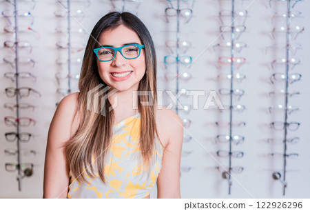 Portrait of happy girl in glasses in an eyeglasses store. Smiling happy girl in eyeglasses with store eyeglasses background Portrait of happy girl in glasses in an eyeglasses store. Smiling happy girl in eyeglasses with store eyeglasses background 122926296