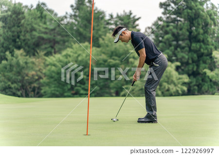 A male golfer trying to put the ball into the cup on a golf course 122926997