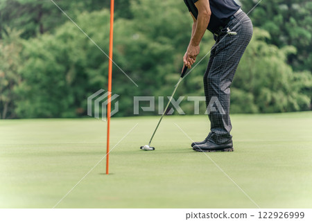 A male golfer trying to put the ball into the cup on a golf course A male golfer trying to put the ball into the cup on a golf course 122926999
