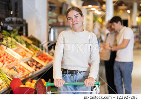 In food store, woman with trolley looking for something on shelf of showcase 122927283