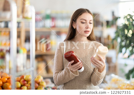 Young woman chooses ketchup or mayonnaise sauces Young woman chooses ketchup or mayonnaise sauces 122927331
