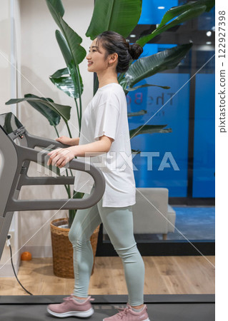 Young woman running on a running machine in an indoor gym Young woman running on a running machine in an indoor gym 122927398