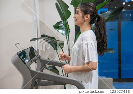 Young woman running on a running machine in an indoor gym Young woman running on a running machine in an indoor gym 122927418
