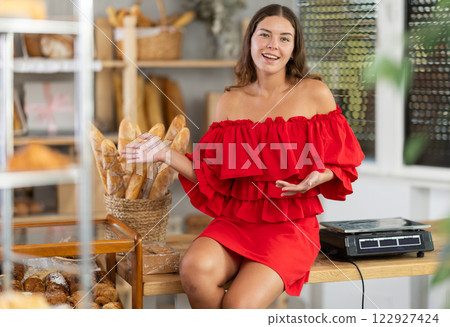 Girl in red dress with bare shoulders is sitting on table in sales area of bakery 122927424