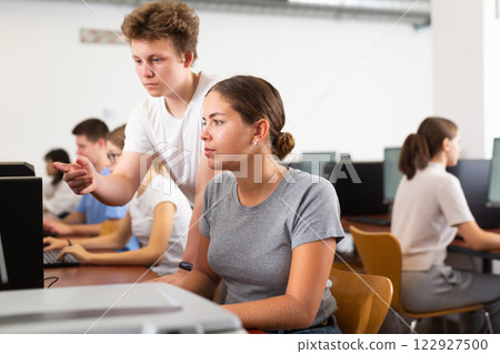 Positive male student explaining the topic to female friend while she is studying computer science on the pc in the classroom 122927500