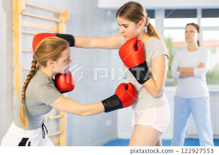 Teenage girl in boxing gloves practicing punches in sparring at self defense training Teenage girl in boxing gloves practicing punches in sparring at self defense training 122927553