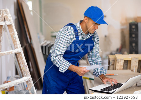 Man builder checking project documentation and using laptop Man builder checking project documentation and using laptop 122927558