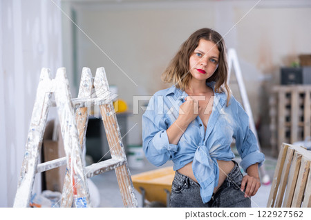 Attractive young woman in denim shirt and shorts posing next to stepladder in refurbished room Attractive young woman in denim shirt and shorts posing next to stepladder in refurbished room 122927562