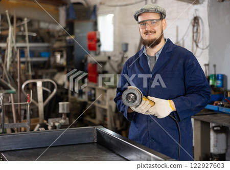 Young man polishing metal part in workshop Young man polishing metal part in workshop 122927603