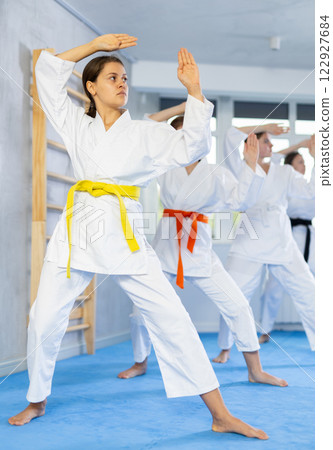 Team of teenage girls in kimonos uses new fighting techniques during karate lessons in gym 122927684