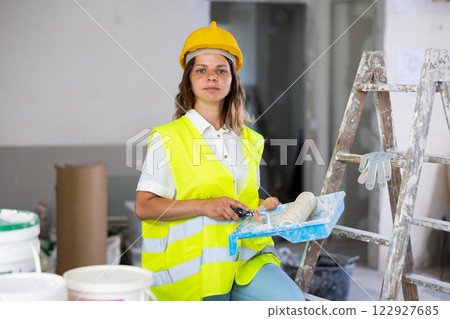 Woman house painter in yellow vest and hardhat in room being renovated 122927685
