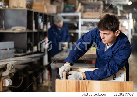 Young worker assembles a wooden table in furniture factory. Work process 122927708