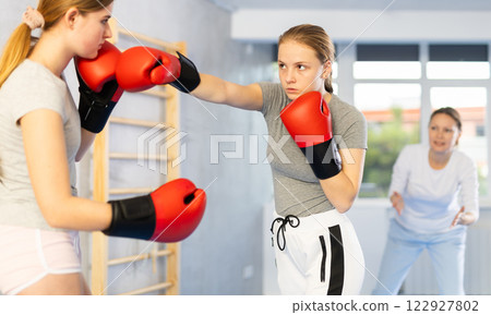 Teenage girl in boxing gloves practicing punches in sparring at self defense training Teenage girl in boxing gloves practicing punches in sparring at self defense training 122927802