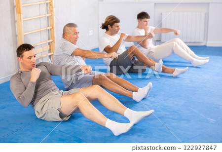 Group of men train abdominal muscles and do punches at the same time during karate or judo training 122927847