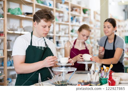 Young woman teaching teen boy and teen girl how to make ceramic cup Young woman teaching teen boy and teen girl how to make ceramic cup 122927865