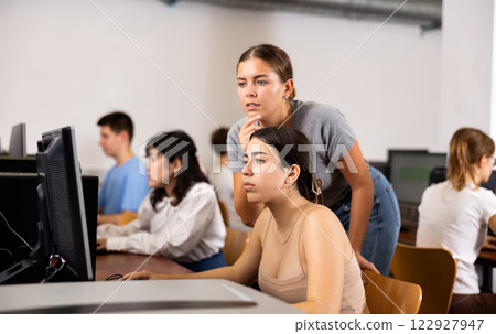 Focused young woman student working with her female friend in computer class, using pc in library 122927947