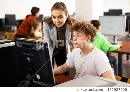 Female teacher and teenage boy looking at monitor of PC 122927996