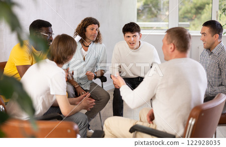 Cheerful male colleagues friendly talking sitting in circle on chairs 122928035