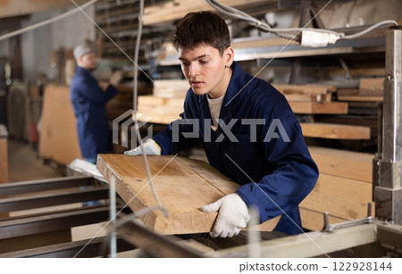Young guy putting wooden board on cutting machine 122928144