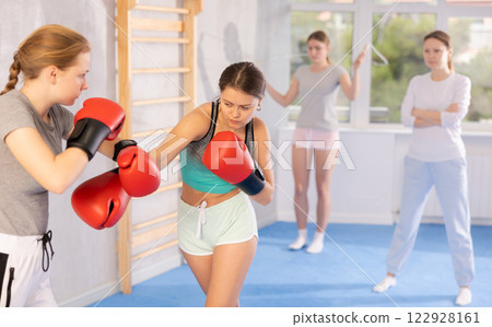 Two teenage girls in boxing gloves learn to box under guidance of trainer in gym 122928161