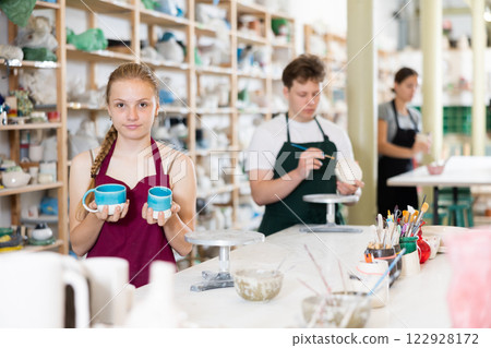 Teenage girl posing with ceramic cup in ceramic workshop 122928172