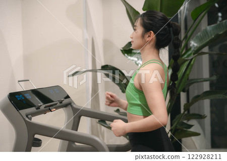 一名身穿訓練服的年輕女子在健身房的跑步機上跑步 一名身穿訓練服的年輕女子在健身房的跑步機上跑步 122928211